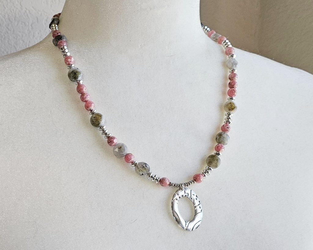 Handcrafted necklace with Rhodochrosite and Labradorite beads, silver accents, and an embossed pewter pendant on a 20-inch strand on bust dispay