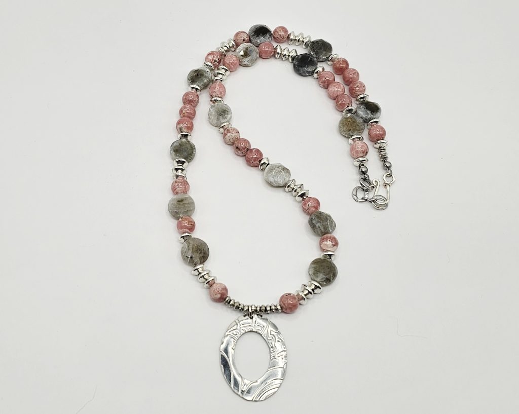 Handcrafted necklace with Rhodochrosite and Labradorite beads, silver accents, and an embossed pewter pendant on a 20-inch strand on flat surface