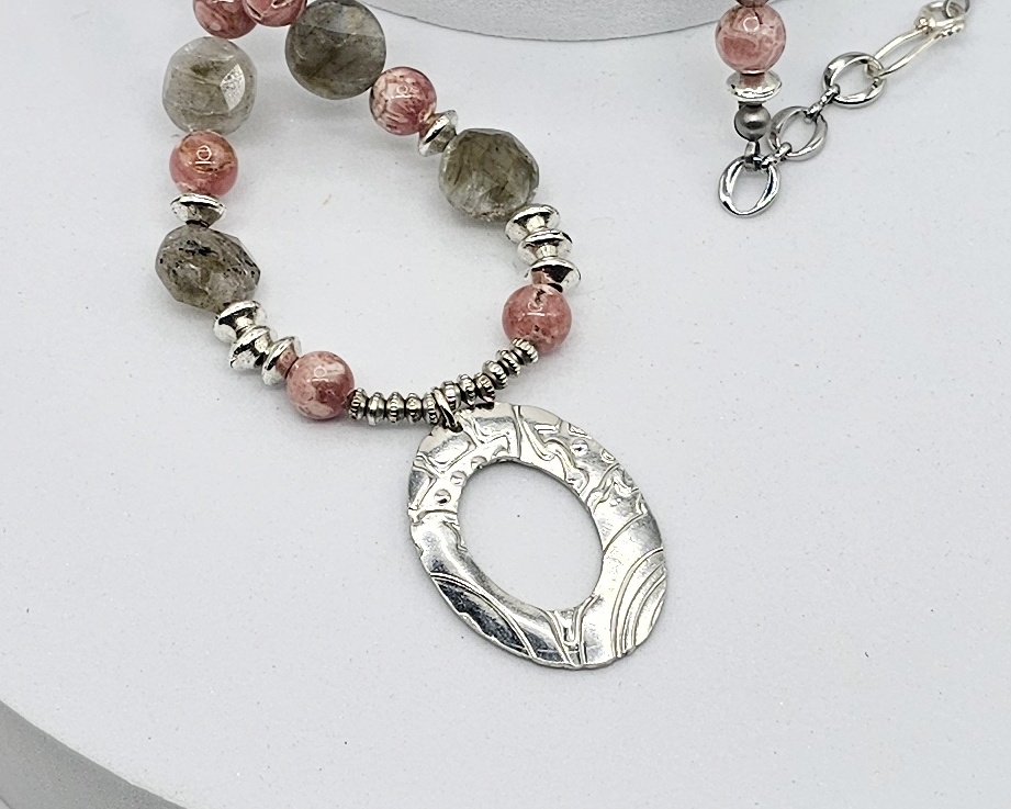 Close-up of pewter pendant on handcrafted necklace with Rhodochrosite and Labradorite beads, silver accents, and an embossed pewter pendant on a 20-inch strand.