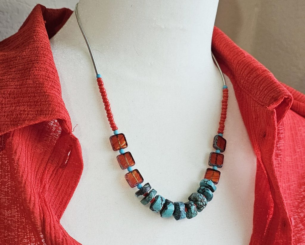 19-20" necklace with rough turquoise rondelle beads and red Czech glass squares, handmade with bold and earthy boho flair displayed on a bodice wearing a red shirt.