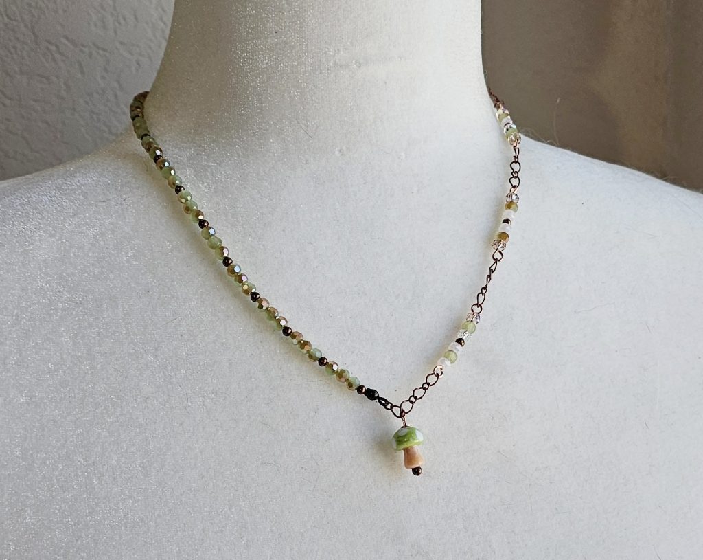 Handmade lampwork mushroom necklace with pink and green faceted crystal beads on copper chain, 19.5 inch adjustable length.