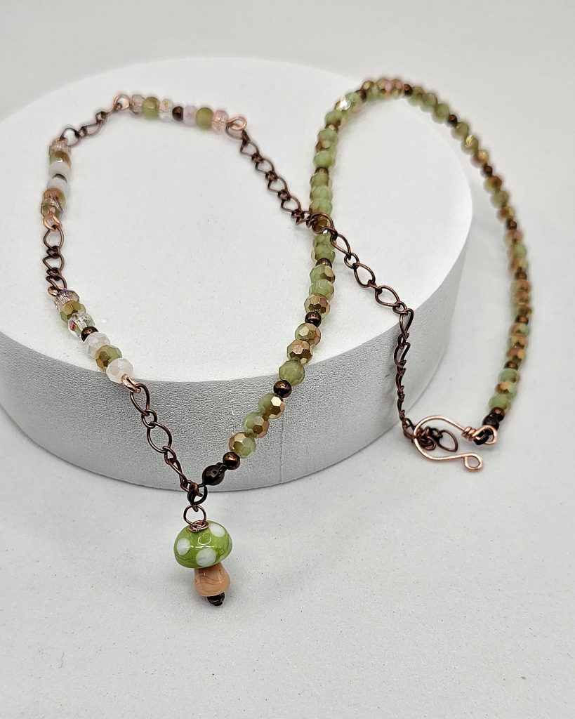 Handmade lampwork mushroom necklace with pink and green faceted crystal beads on copper chain, 19.5 inch adjustable length.