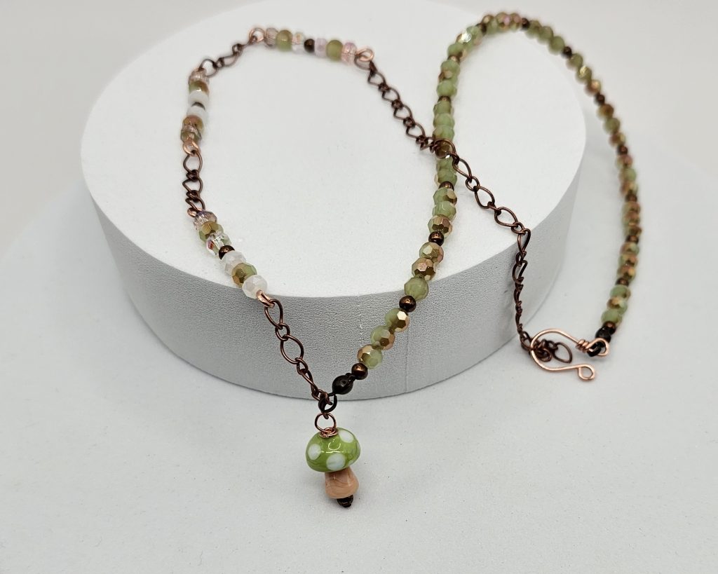Handmade lampwork mushroom necklace with pink and green faceted crystal beads on copper chain, 19.5 inch adjustable length.