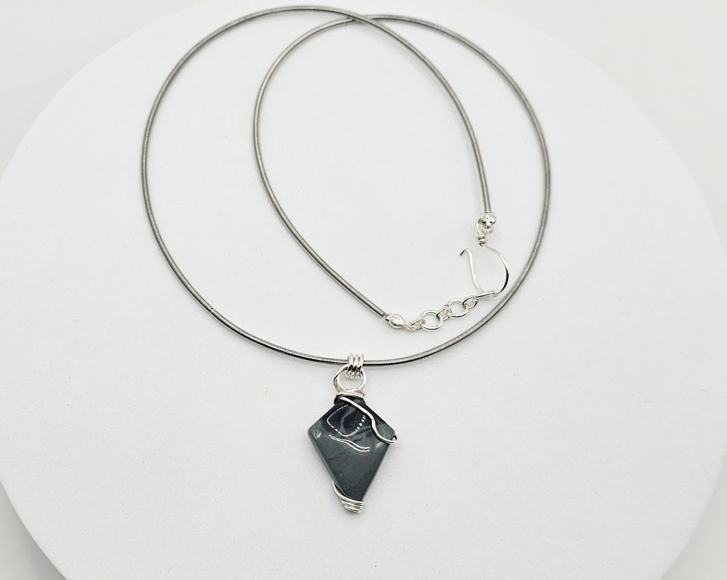 One-of-a-kind handmade wire wrapped dark stone pendant necklace with silver-tone detailing on an adjustable 20-inch chain.