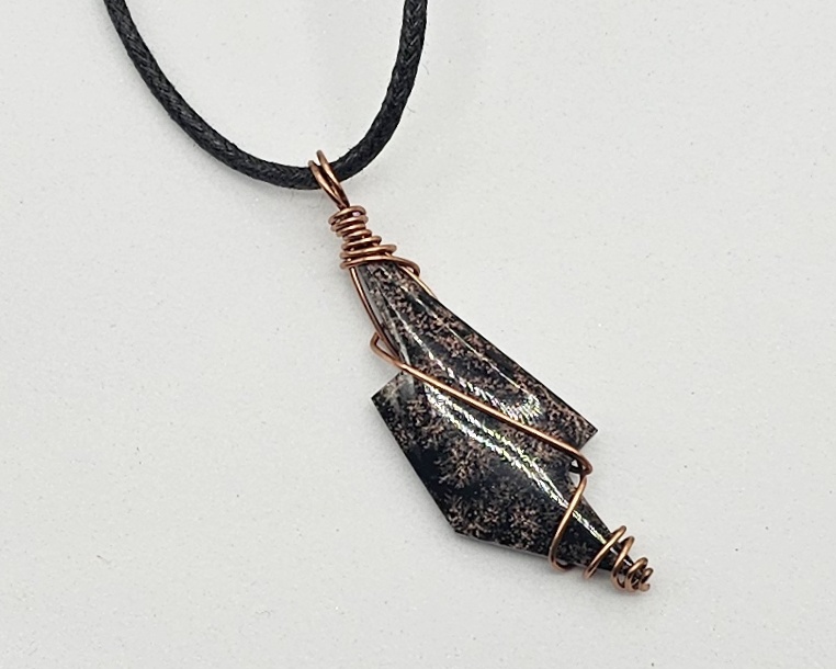 Handmade obsidian pendant necklace wrapped in copper wire on a black waxed cotton cord with a geometric stone design.