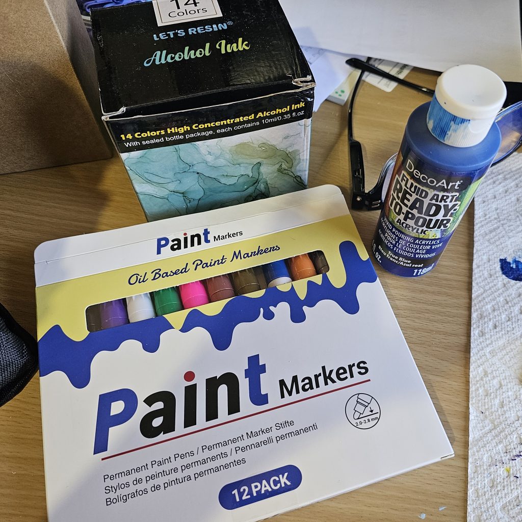 Oil based paint markers in 12 colors, box of Let's Resin alcohol ink, bottle of blue DecoArt acrylic pour paint