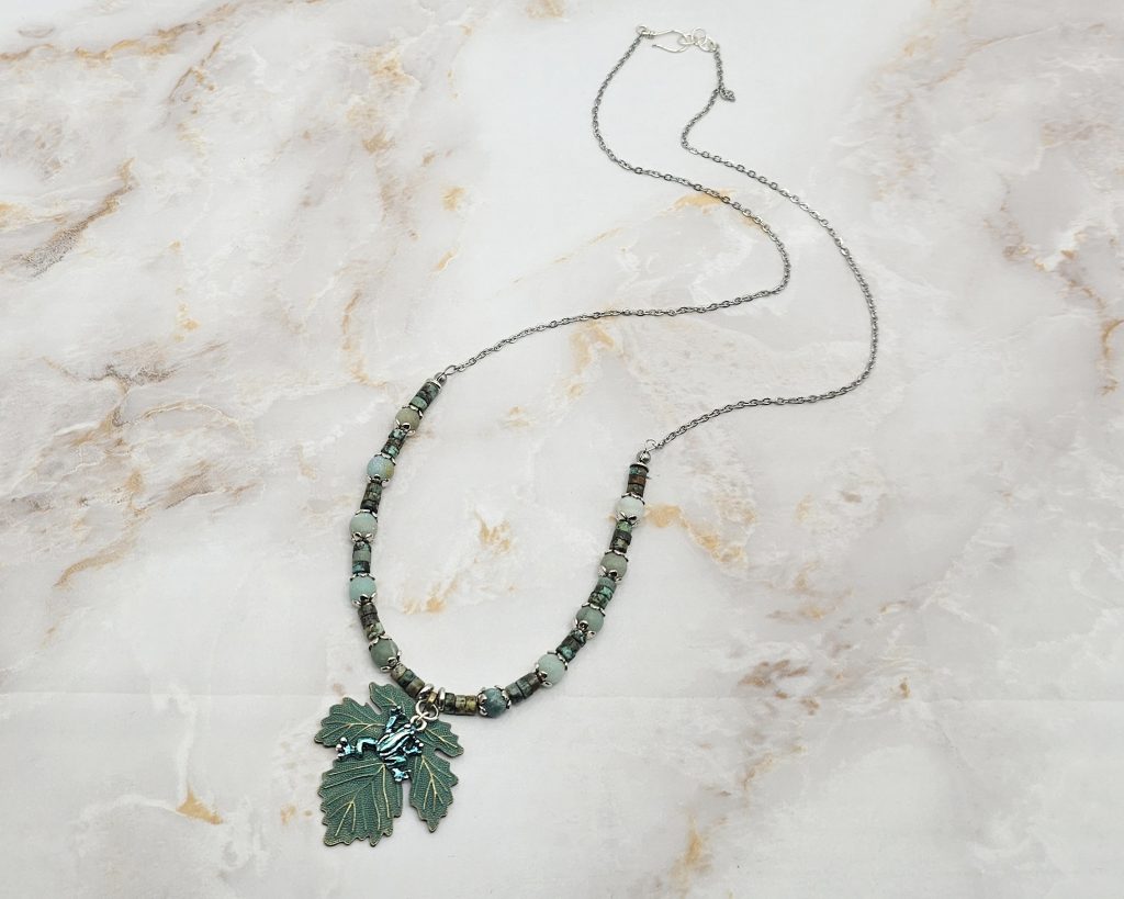 Handmade African turquoise jasper and amazonite necklace with antique bronze leaf pendant and hand-colored antique silver frog charm.