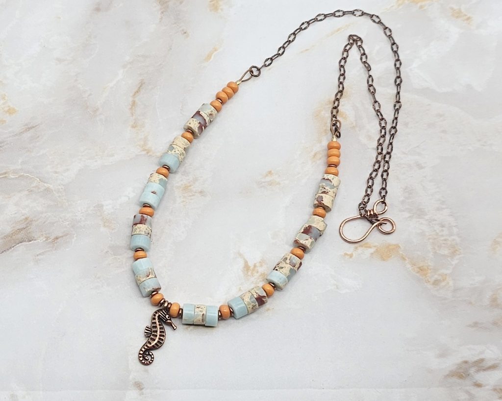 Handmade 19-inch necklace with impression jasper beads, orange glass accents, copper spacers, and a copper seahorse charm.