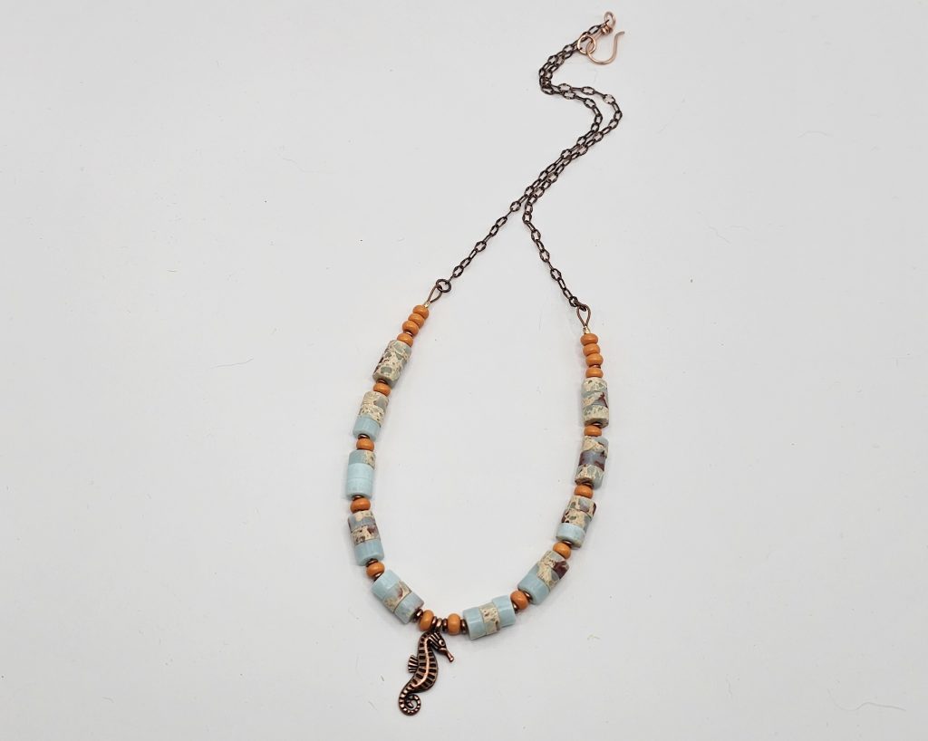 Handmade 19-inch necklace with impression jasper beads, orange glass accents, copper spacers, and a copper seahorse charm.