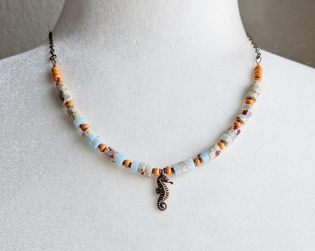 Handmade 19-inch necklace with impression jasper beads, orange glass accents, copper spacers, and a copper seahorse charm.